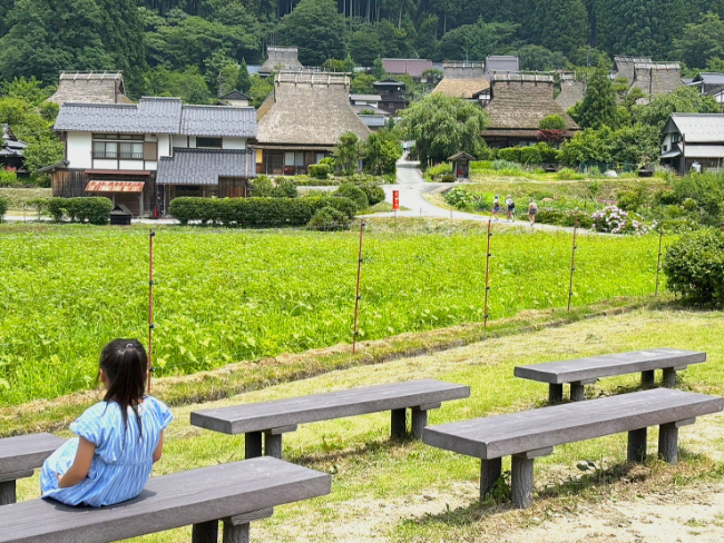 かやぶきの里を見ながら休憩する子ども