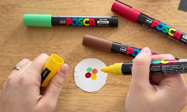 丸く切った白い画用紙にペンで色を塗っている作り方の工程