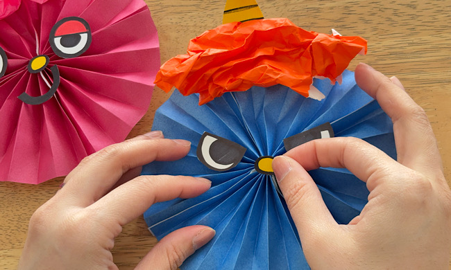 折り紙のペーパーファンに目や鼻を貼り付ける様子